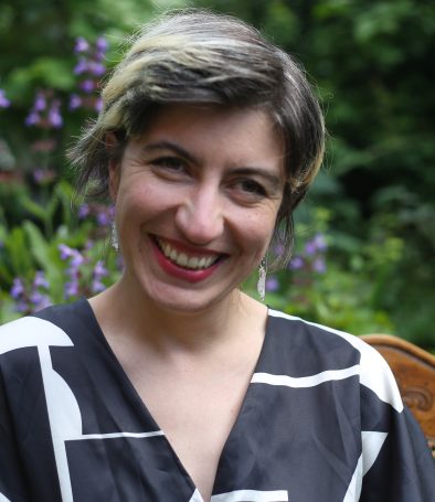 Woman with short black and grey hair in a black and white shirt in a garden.